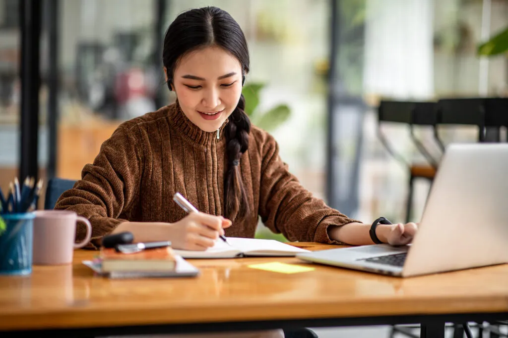 A young, female-presenting college intern works at a table using a laptop computer