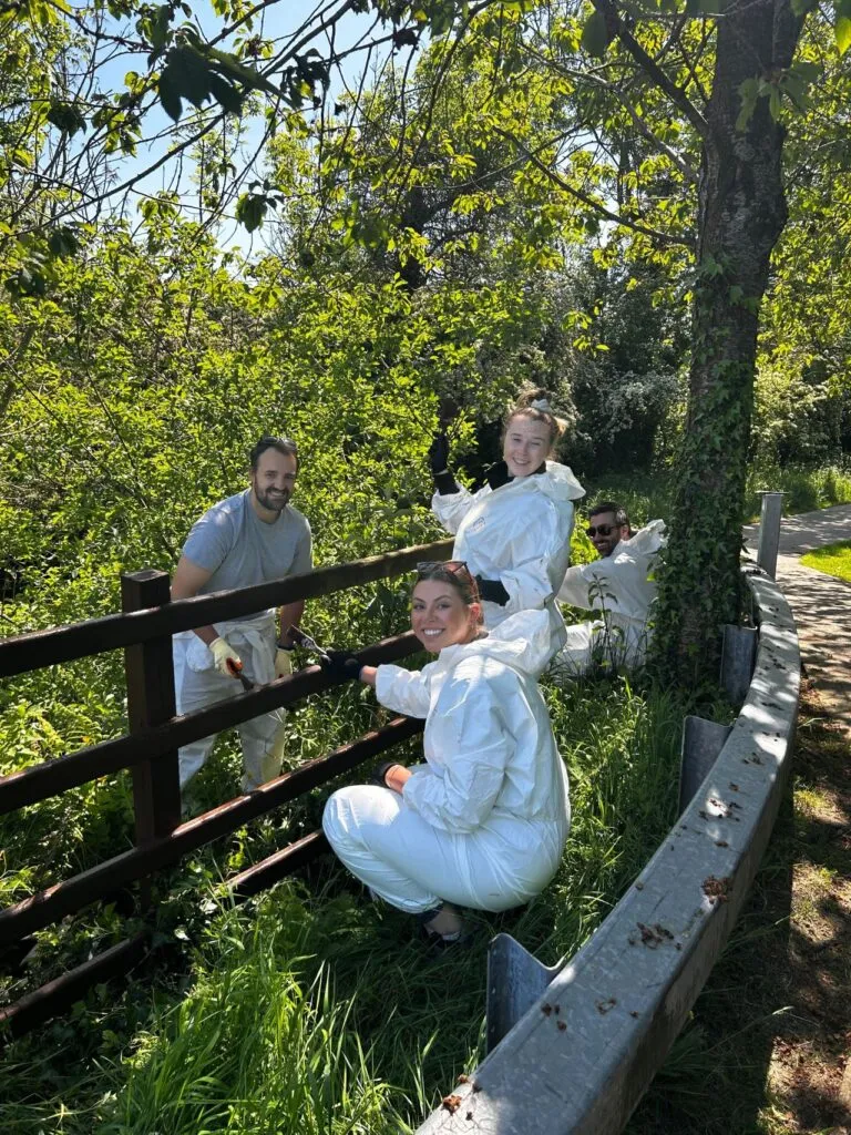 Four Apex Fintech Solutions UK employees are viewed outside. They are wearing white protective gear as they repair and paint a fence.